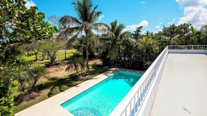 A swimming pool with a white deck and a white railing, surrounded by lush greenery and palm trees. - Private Villa with Pool, Chef, and Golf Cart, Punta Cana (Punta Cana)