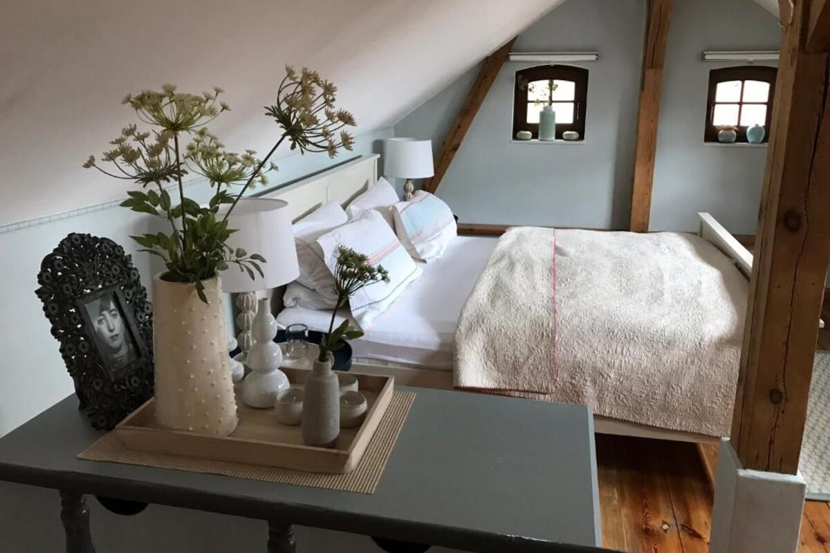 Quarto com cama, mesa de cabeceira, abajur e objetos decorativos.