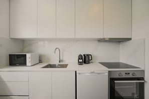 Een moderne keuken met witte kastjes, een magnetron, een waterkoker en een vaatwasser.