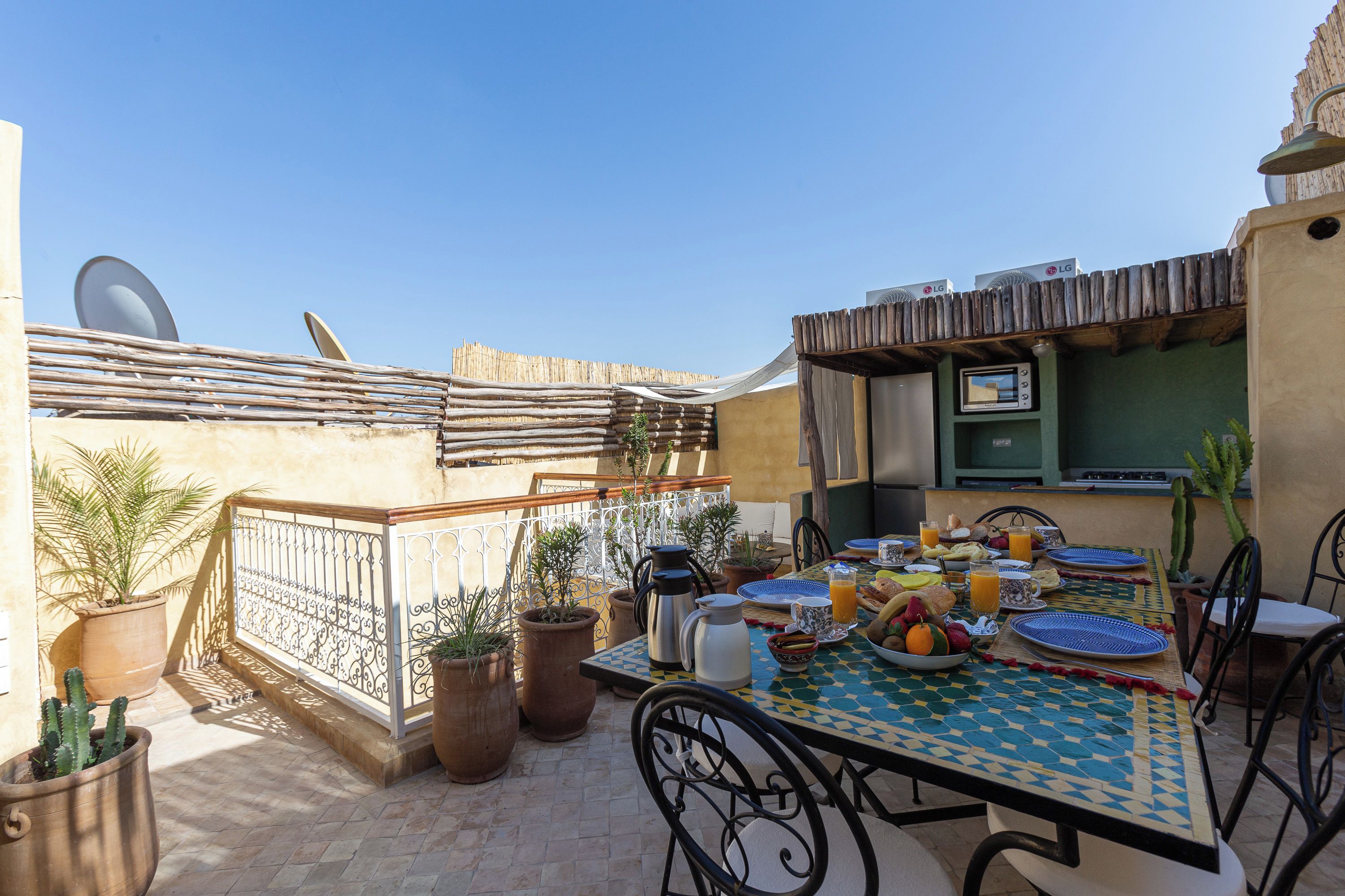 An outdoor dining area with a table set for breakfast, surrounded by potted plants and a wooden fence.