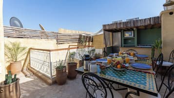 An outdoor dining area with a table set for breakfast, surrounded by potted plants and a wooden fence.