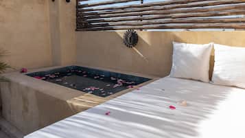 Een kamer met een bed, een klein bad met rozenblaadjes en een houten hek.