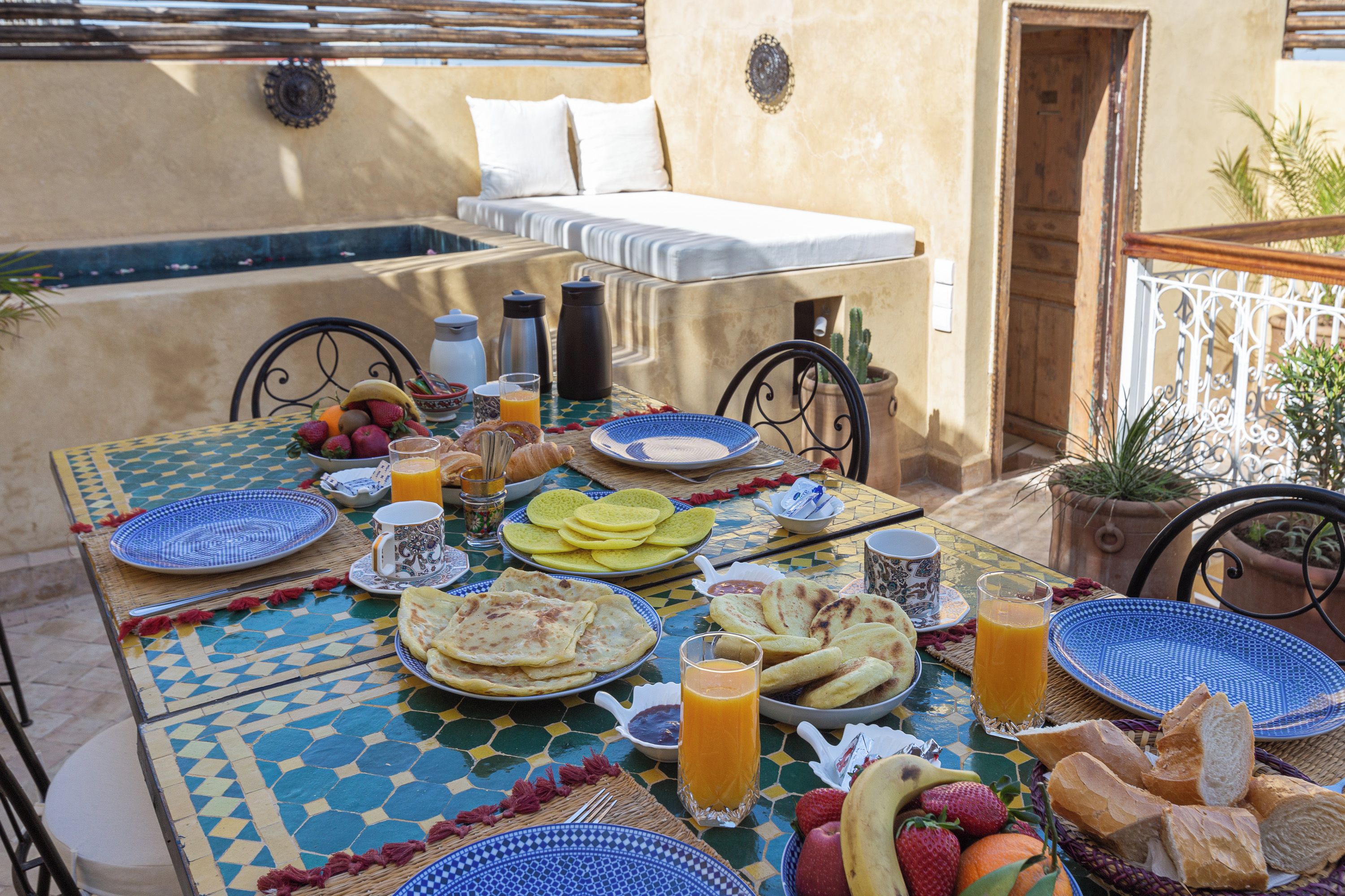 An outdoor dining area with a table set for breakfast, including fruits, bread, and beverages.