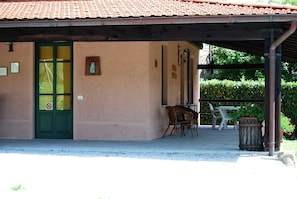 A building with a green door, a small outdoor seating area with chairs and a table, and a trash bin. - Hillside Villa in Pistoia Hills (San Marcello Piteglio)