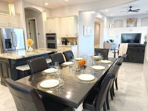 A modern kitchen with a dining area, featuring a marble countertop, stainless steel appliances, and a dark dining table set for six. - AllStar Retreat! PickleBall/Soccer/Pool/Waterslide/Spa/Splash Pad/Putting Greens (Queen Creek)