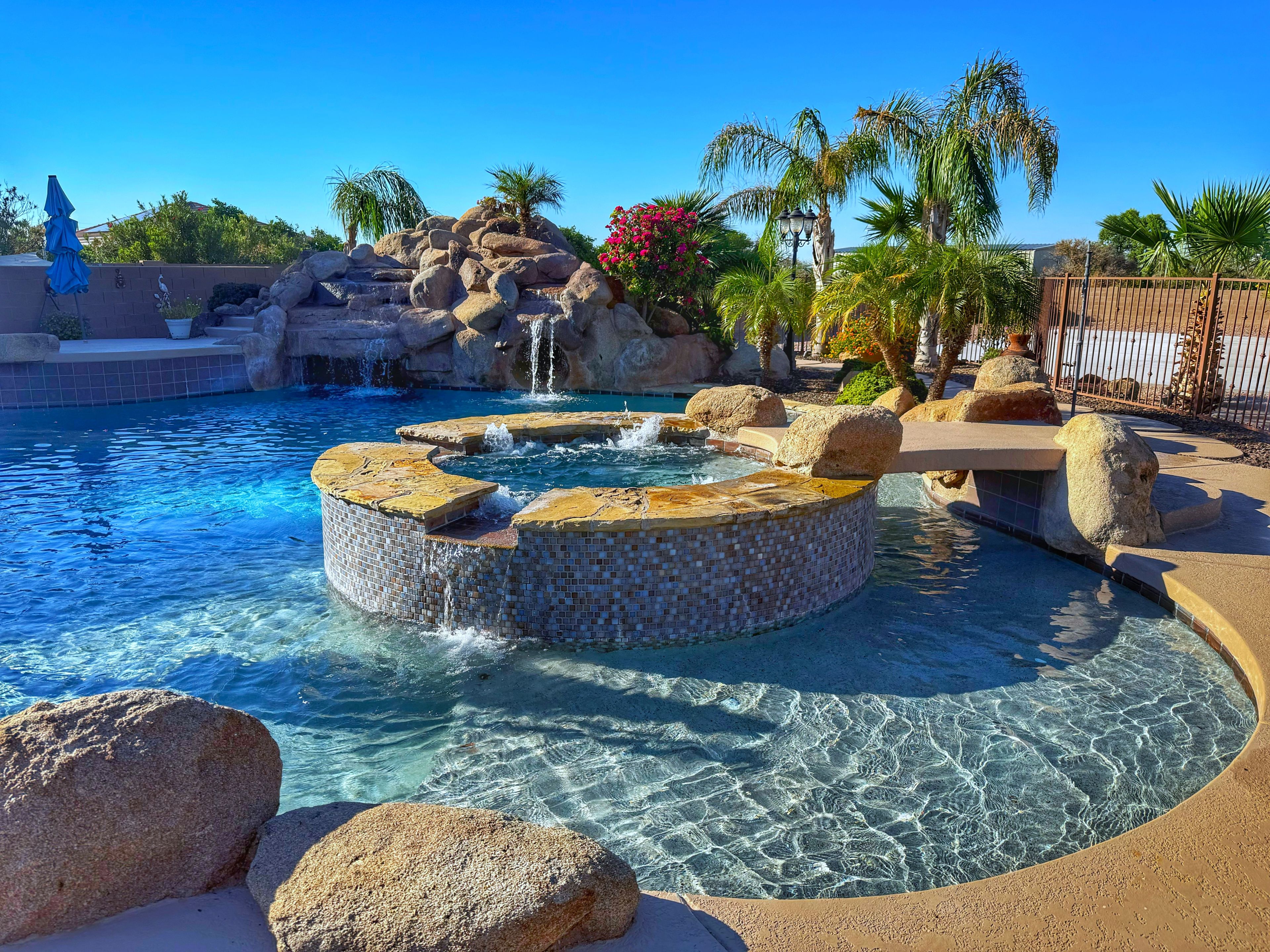 A pool with a hot tub, surrounded by rocks and palm trees.