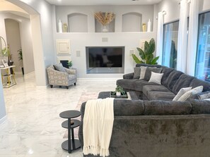 Ein modernes Wohnzimmer mit einem grauen Ecksofa, einem kleinen runden Tisch und einem Flachbildfernseher über einem Kamin.