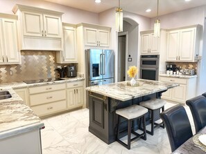 A modern kitchen with marble countertops, stainless steel appliances, and a central island with bar stools. - AllStar Retreat! PickleBall/Soccer/Pool/Waterslide/Spa/Splash Pad/Putting Greens (Queen Creek)