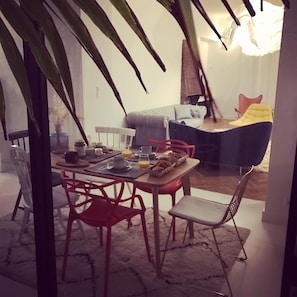A dining area with a table set for breakfast, chairs, and a sofa in the background. - Maison Caju (La Rochelle)