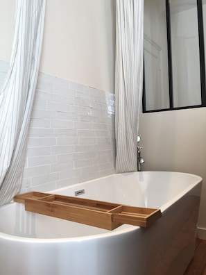 A bathroom with a white bathtub, wooden sideboard, and a tiled wall. - Maison Caju (La Rochelle)