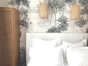 A bedroom with a bed, white pillows, a wooden headboard, and a wall with a nature-themed mural. - Maison Caju (La Rochelle)