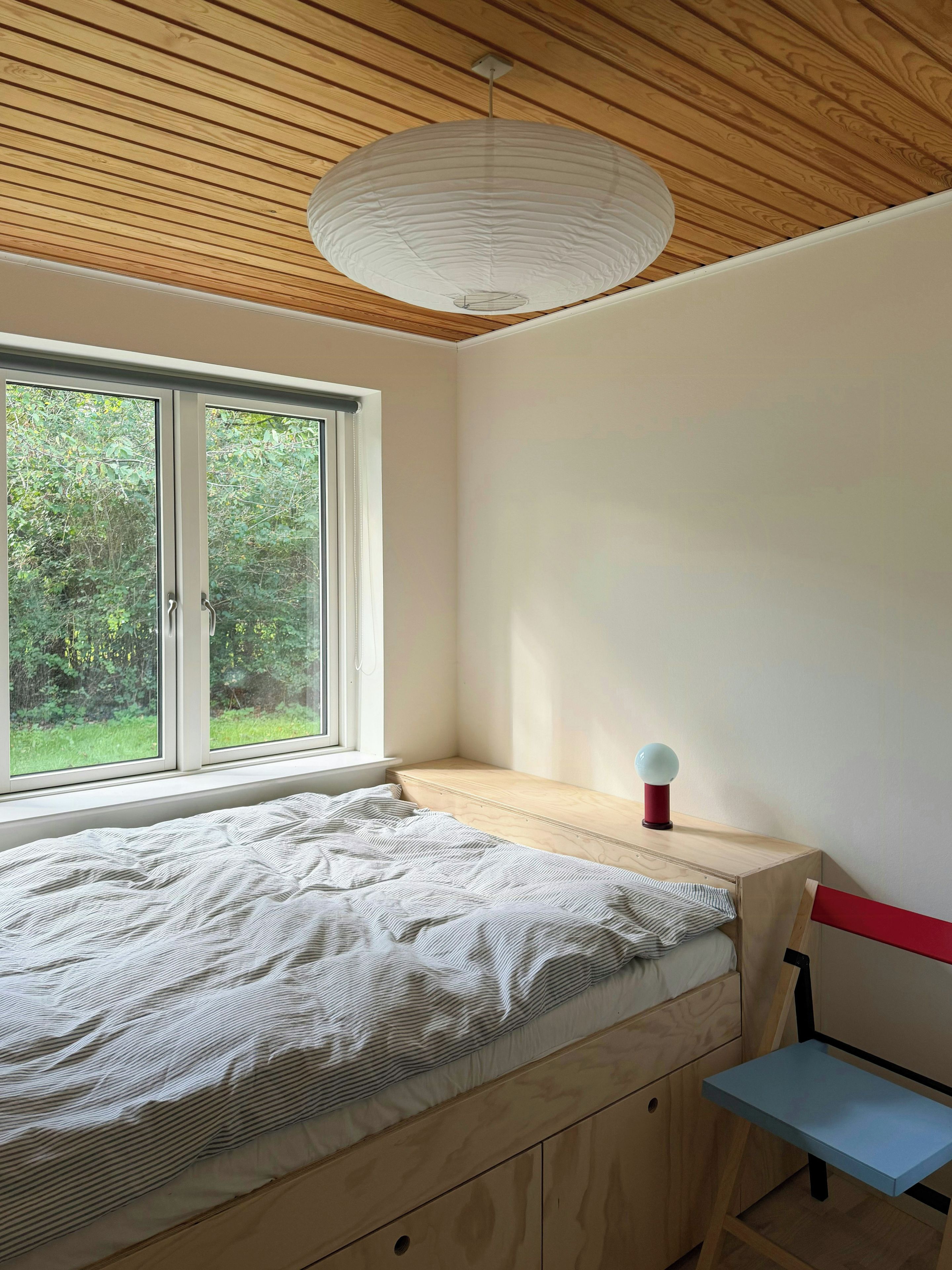 A bedroom with a bed, a window, a bedside table, and a hanging light fixture.
