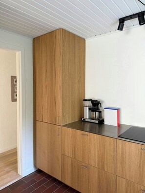 A kitchen with wooden cabinets, a coffee machine, and a red and white appliance on the counter. - Renovated 1970s house by nature reserve (Vejby)