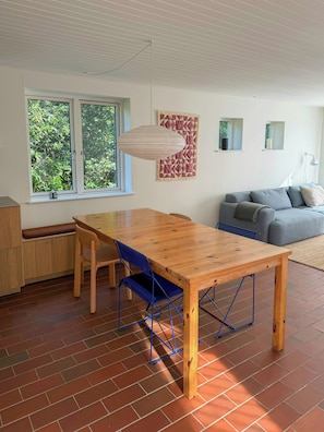 A dining area with a wooden table and blue chairs, a sofa, and a quilt on the wall. - Renovated 1970s house by nature reserve (Vejby)
