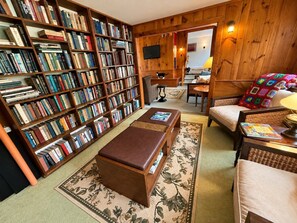 A cozy library with bookshelves, a comfortable seating area, and a television. - Wiley Inn | Mountain Retreat with Hot Tub & Sauna (Peru)