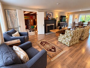 A spacious living room with a fireplace, a dining area with a table and chairs, and a large window with a view. - Wiley Inn | Mountain Retreat with Hot Tub & Sauna (Peru)