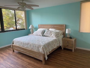 A bedroom with a wooden bed, two bedside tables with lamps, a ceiling fan, and a window with a view of trees. - Cozy 2-bedroom condo with AC in nice Siesta Key (Siesta Key)