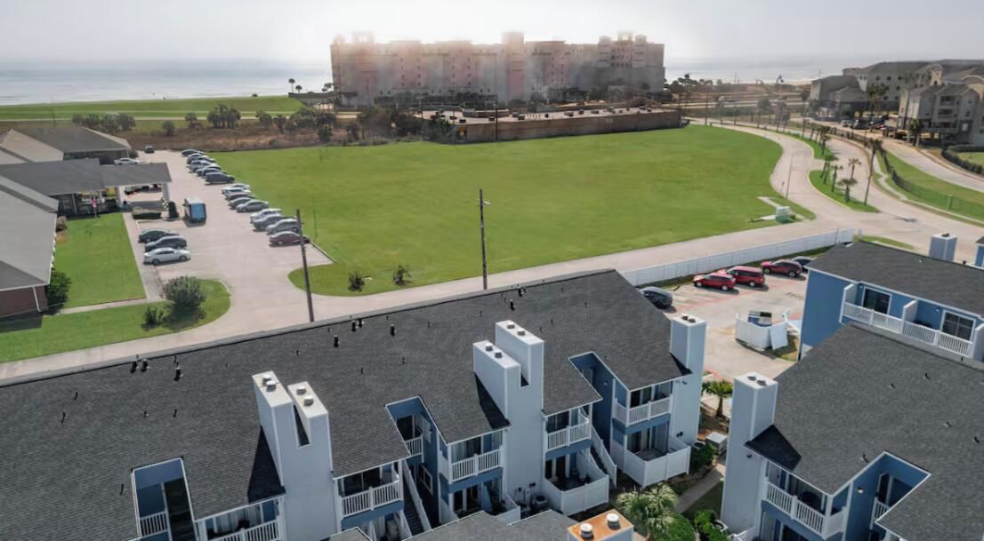Zona residencial con edificios de varios pisos, un estacionamiento y un amplio campo cubierto de césped.