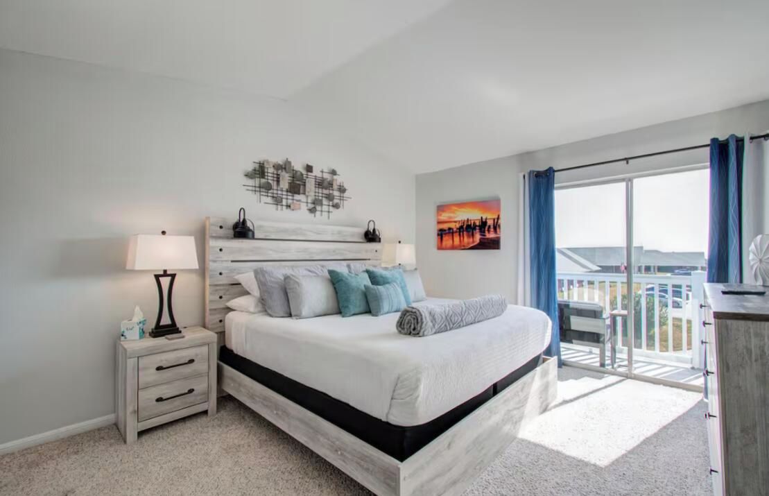 A bedroom with a bed, nightstand, and a view of the outdoors.