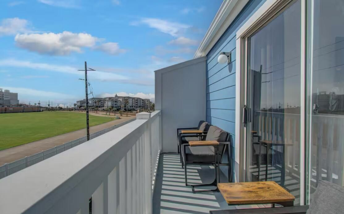 Een balkon met uitzicht op een sportveld, een zithoek met stoelen en een tafel, en een gebouw met grote ramen.