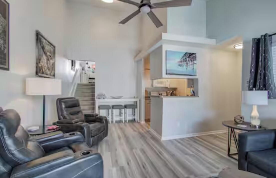 A living room with a sofa, a chair, a dining area with a table and chairs, and a kitchen area with a microwave.