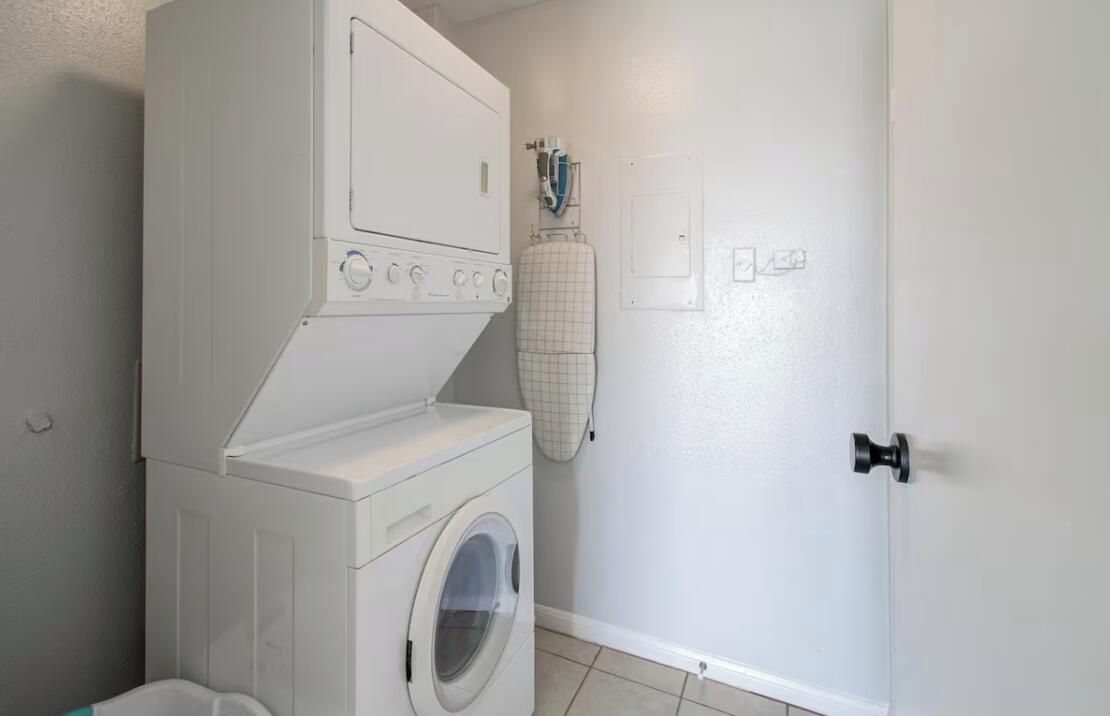 A laundry room with a front-loading washer and dryer, a drying rack, and a door with a handle.