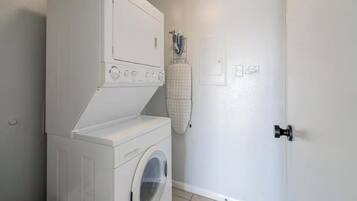 A laundry room with a front-loading washer and dryer, a drying rack, and a door with a handle.