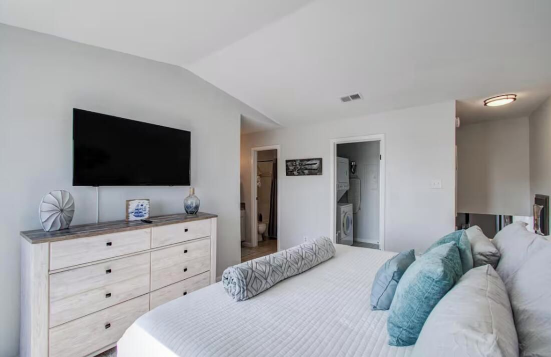 Een slaapkamer met een bed, een kaptafel, een aan de muur bevestigde televisie en een deur naar een andere kamer.
