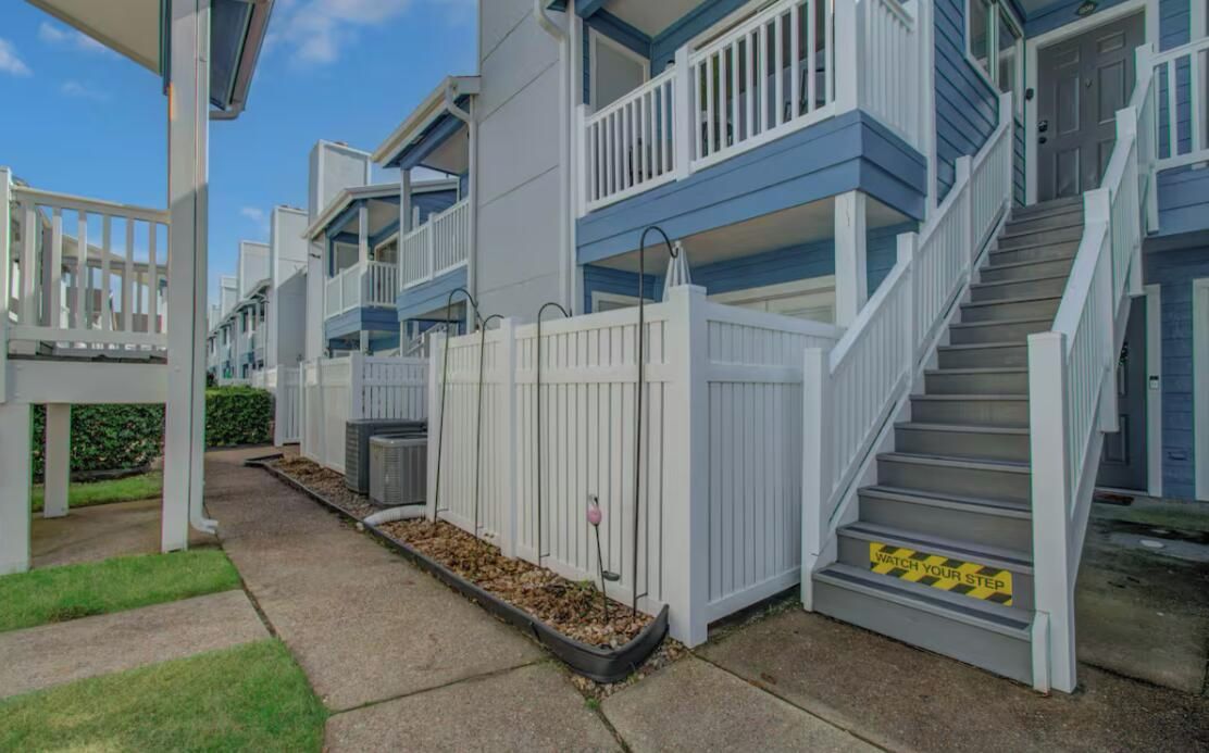 A residential building with a white fence, a gated entrance, and a staircase leading to the entrance.