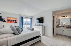 A bedroom with a bed, a TV, a dresser, and a bathroom with a mirror and sink. - Palms Escape (Galveston)