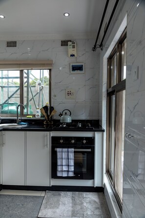 A modern kitchen with white cabinetry, a black countertop, a stove, and an oven. - Chic & Cozy Studio Retreat in Lusaka | Peaceful City Escape. (Lusaka)