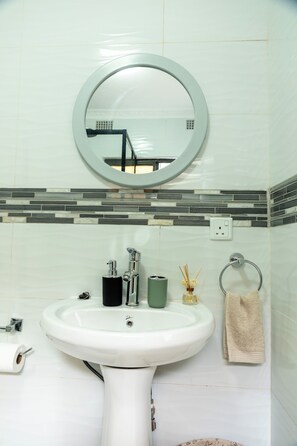 A bathroom with a white sink, a mirror, a towel rack, and a soap dispenser. - Chic & Cozy Studio Retreat in Lusaka | Peaceful City Escape. (Lusaka)
