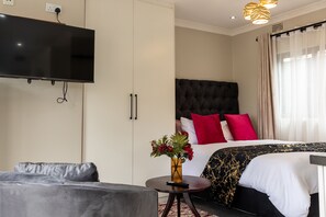 Ein Hotelzimmer mit Bett, einer Couch, einem Fernseher und einer Blumenvase.