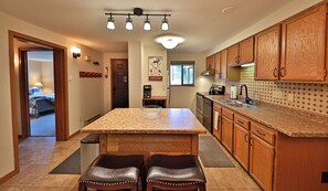 A kitchen with wooden cabinets, a granite countertop, and a dining area with two leather chairs. - Cozy Winter Park Condo in Forest + Walk to Town! (Winter Park)