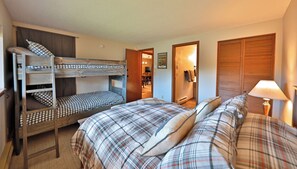 A room with bunk beds, a single bed, a bedside table with a lamp, and a door leading to a hallway. - Cozy Winter Park Condo in Forest + Walk to Town! (Winter Park)