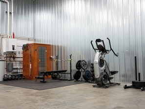 Ein Fitnessraum mit Trainingsgeräten, einem Durchlauferhitzer und einer Holzkabine.