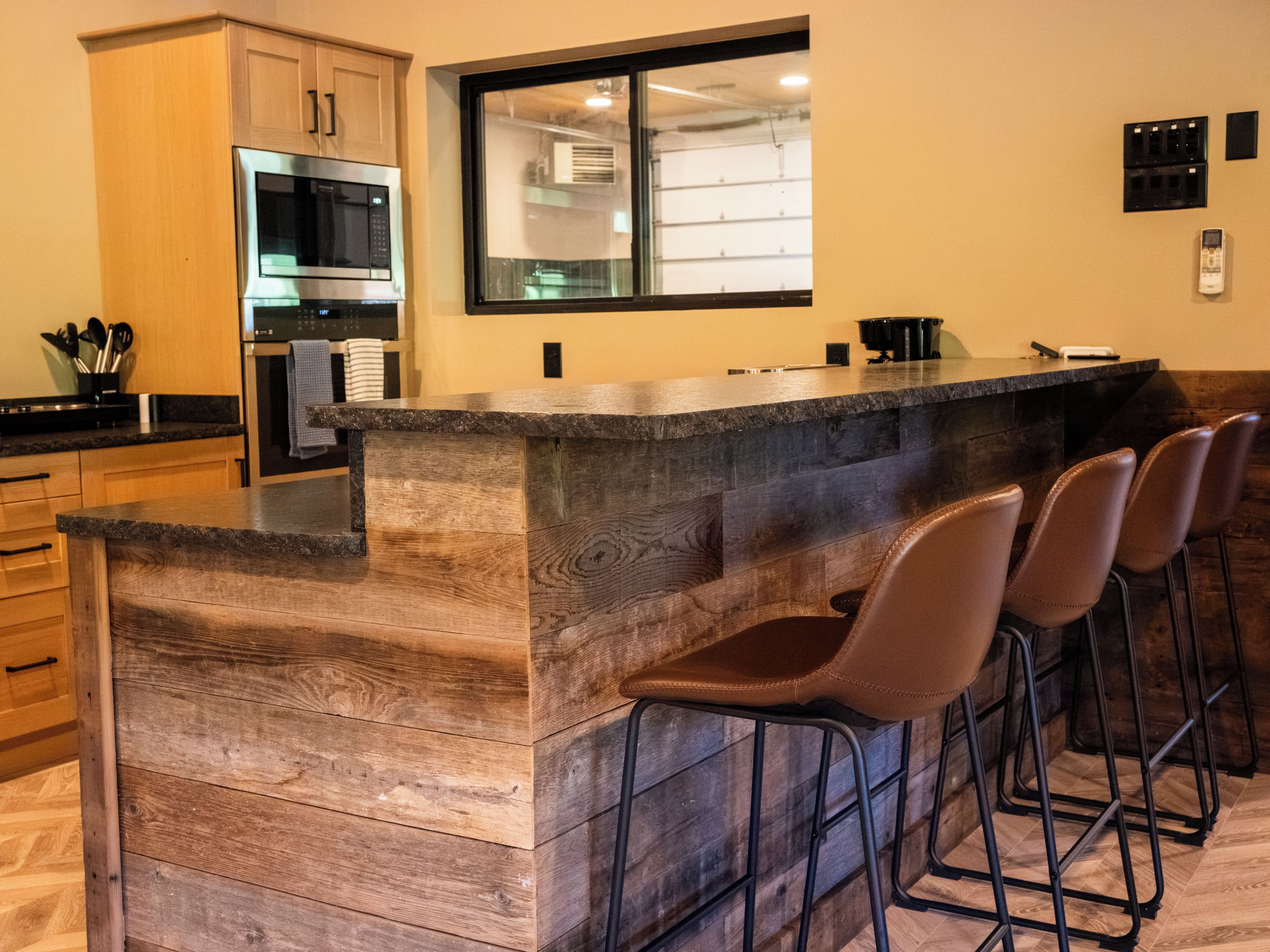 A kitchen with a bar area, wooden cabinets, a microwave, and a large window.