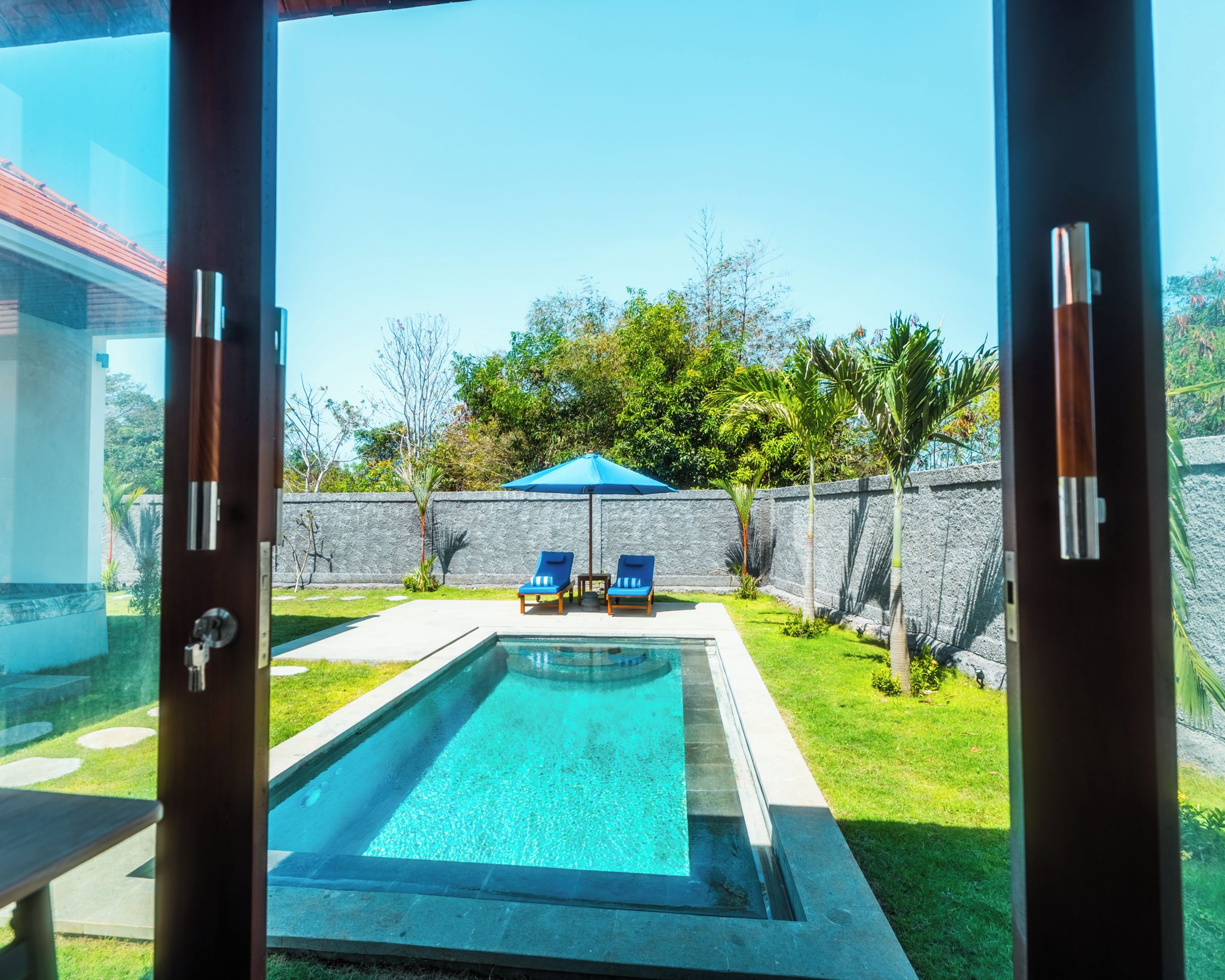 A swimming pool with two lounge chairs and a blue umbrella.