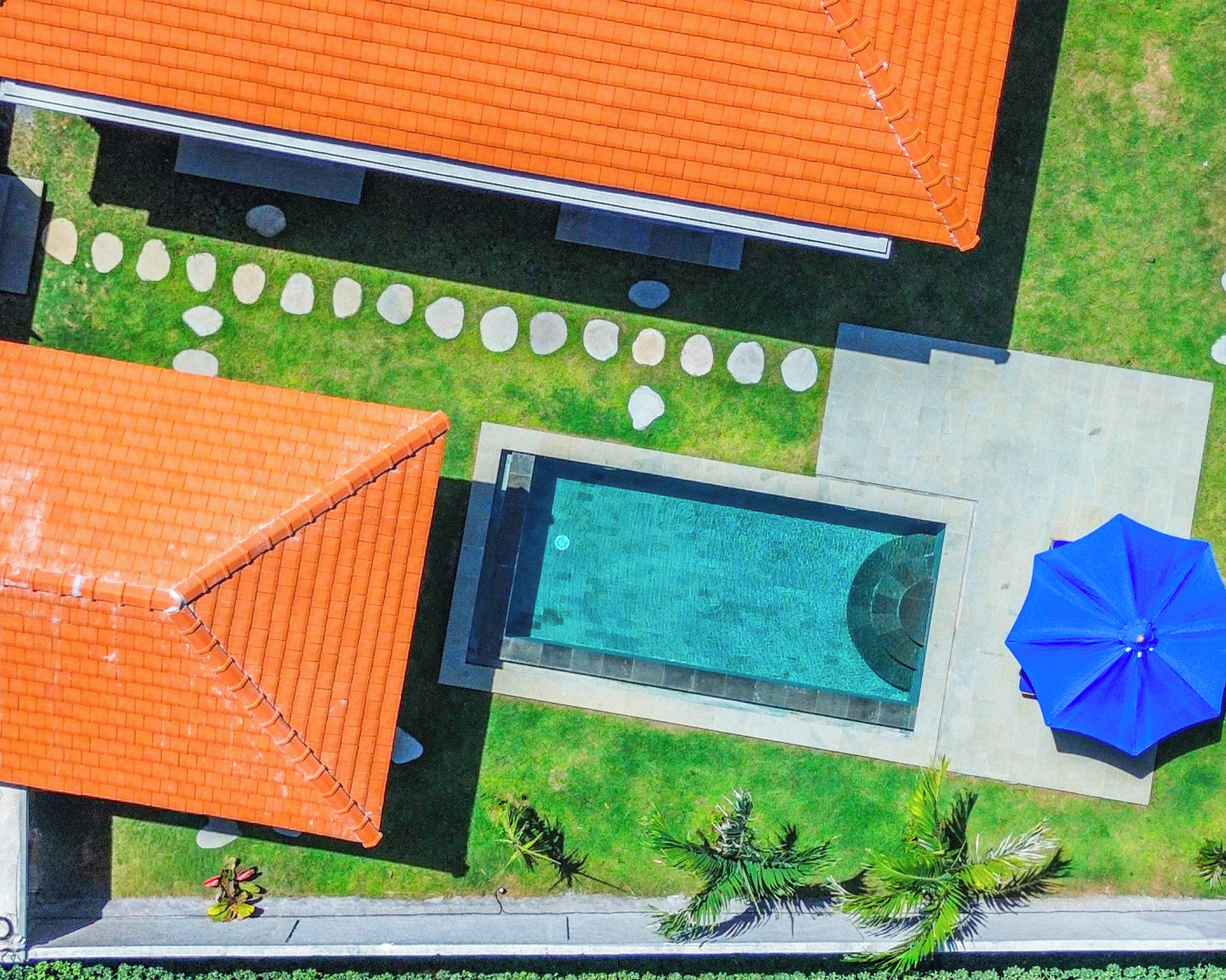 An aerial view of a property with a swimming pool, a blue umbrella, and a garden with a pathway.