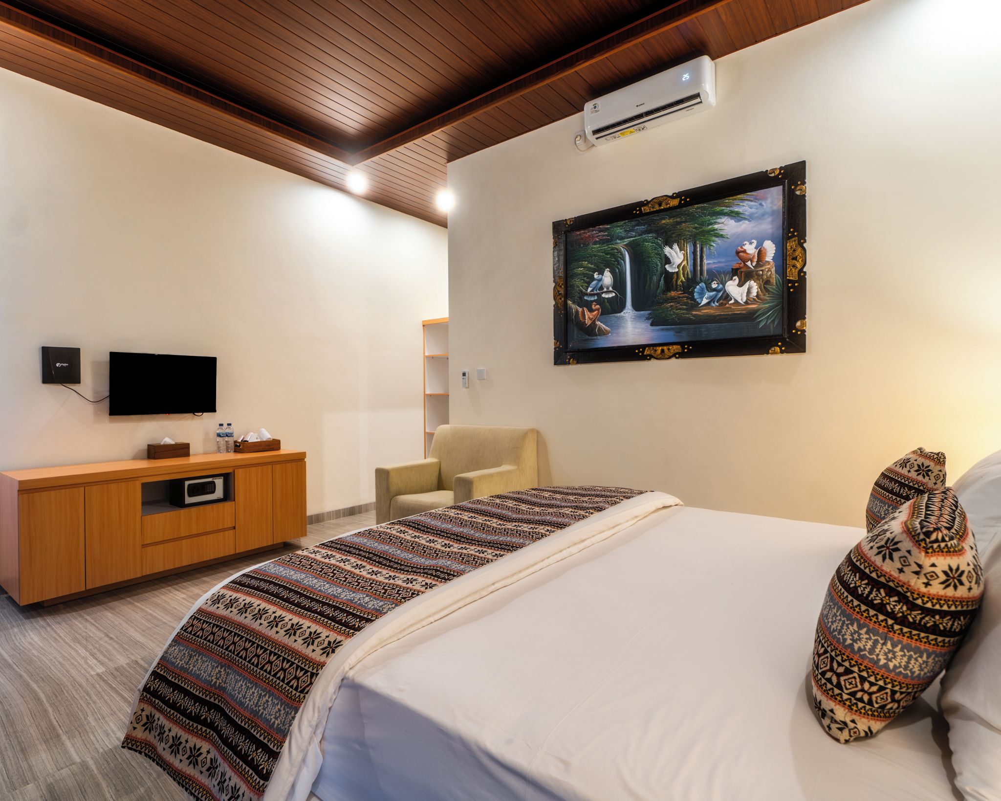 A hotel room with a bed, a television, a painting, and a wooden cabinet.