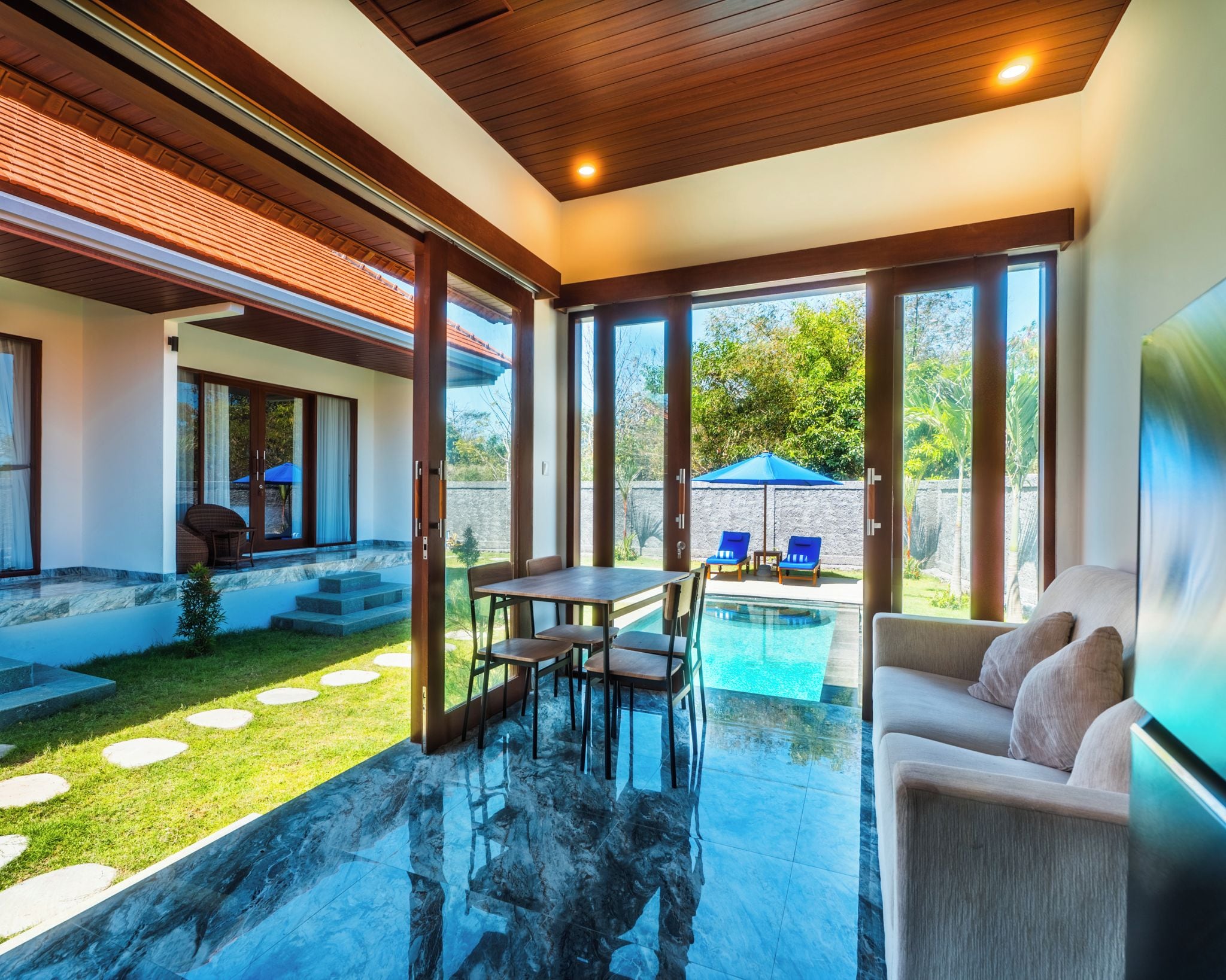 Interior moderno com porta de vidro que dá para uma área de piscina, mesa de jantar com cadeiras e um sofá.