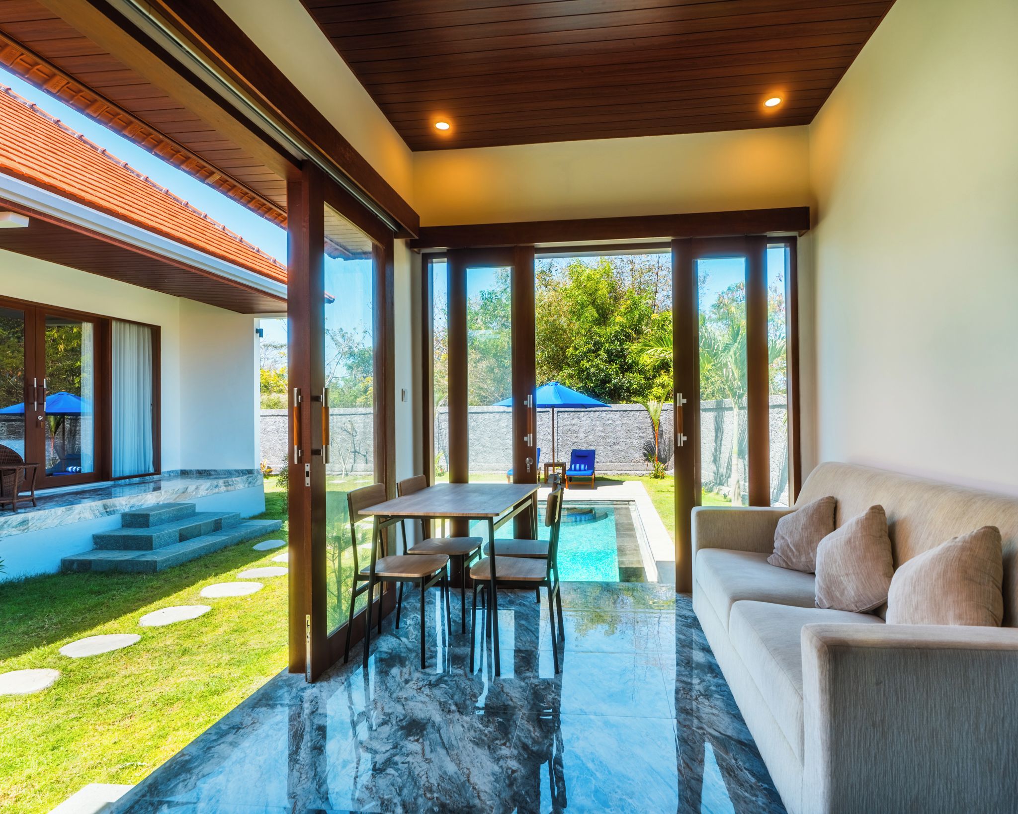 A modern interior with a glass door leading to a pool area, a dining table, and a sofa.