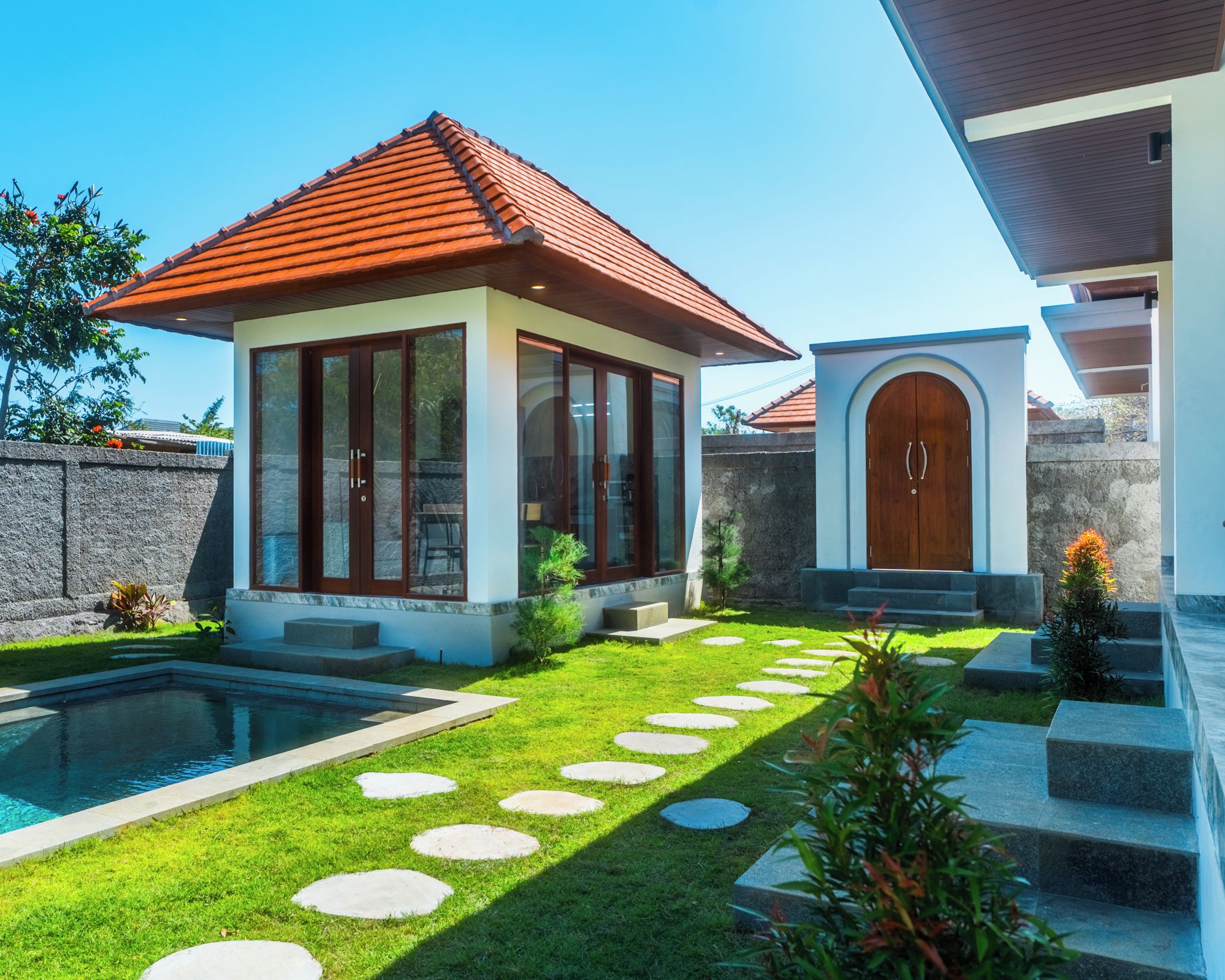 A modern house with a swimming pool, a well-maintained lawn, and a stone wall.