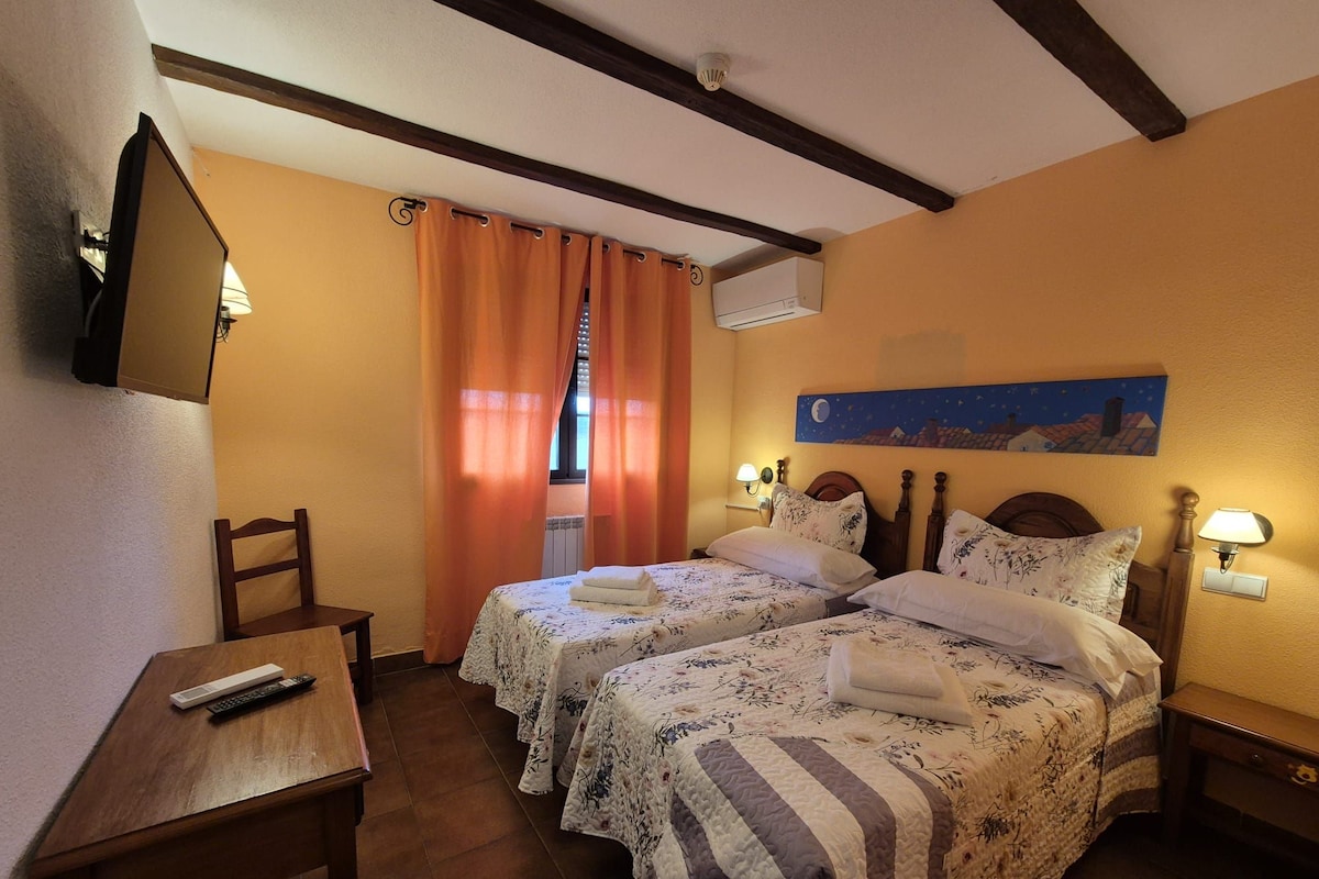 A hotel room with two beds, a desk, a chair, a TV, and a painting on the wall.