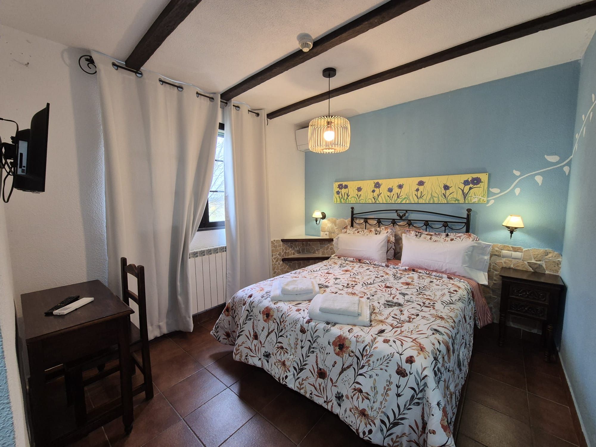 Un dormitorio con cama, escritorio, silla, ventana con cortinas, lámpara de pared y lámpara del techo.