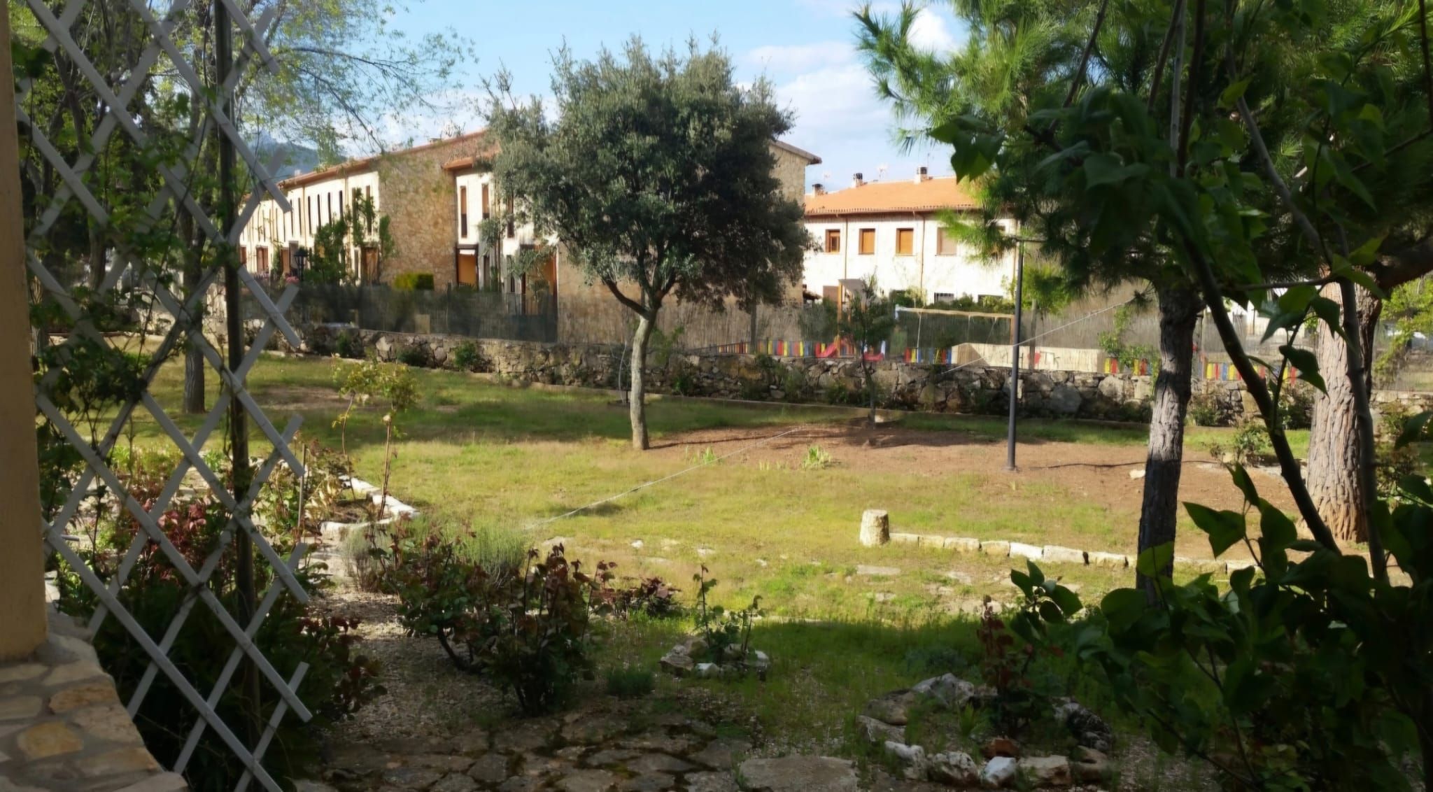 Un cortile con un vialetto in pietra, una zona verdeggiante e un edificio con tetto in tegole sullo sfondo.