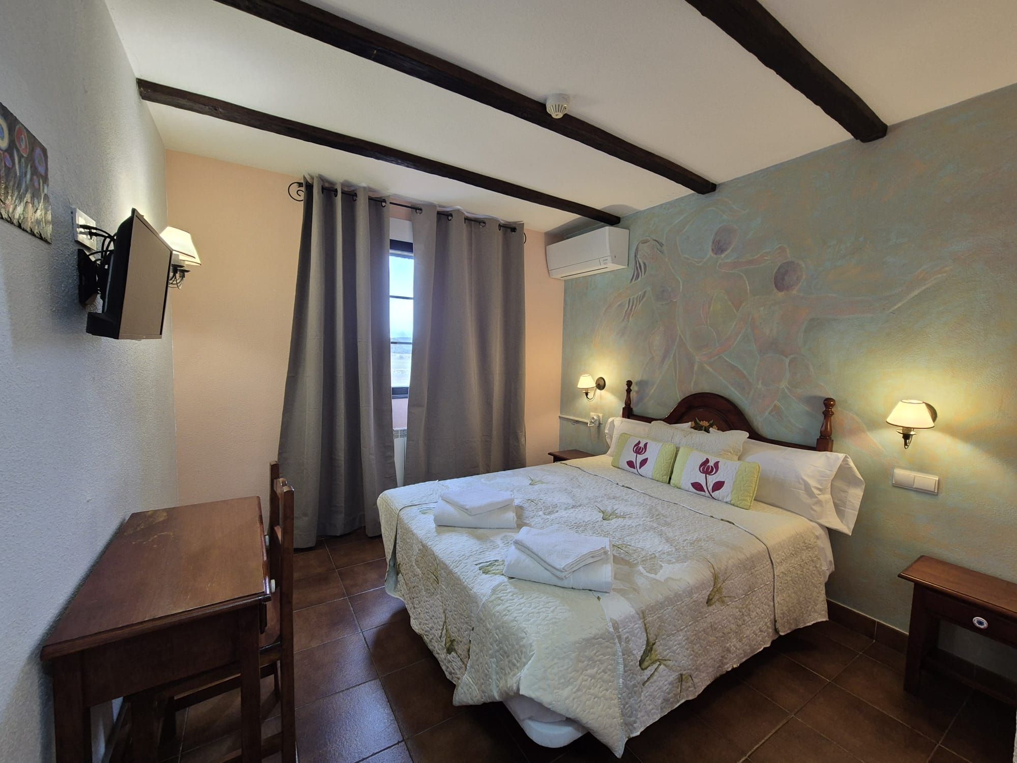 Un dormitorio con una cama, dos lámparas de noche, un escritorio, una silla y una ventana con cortinas.