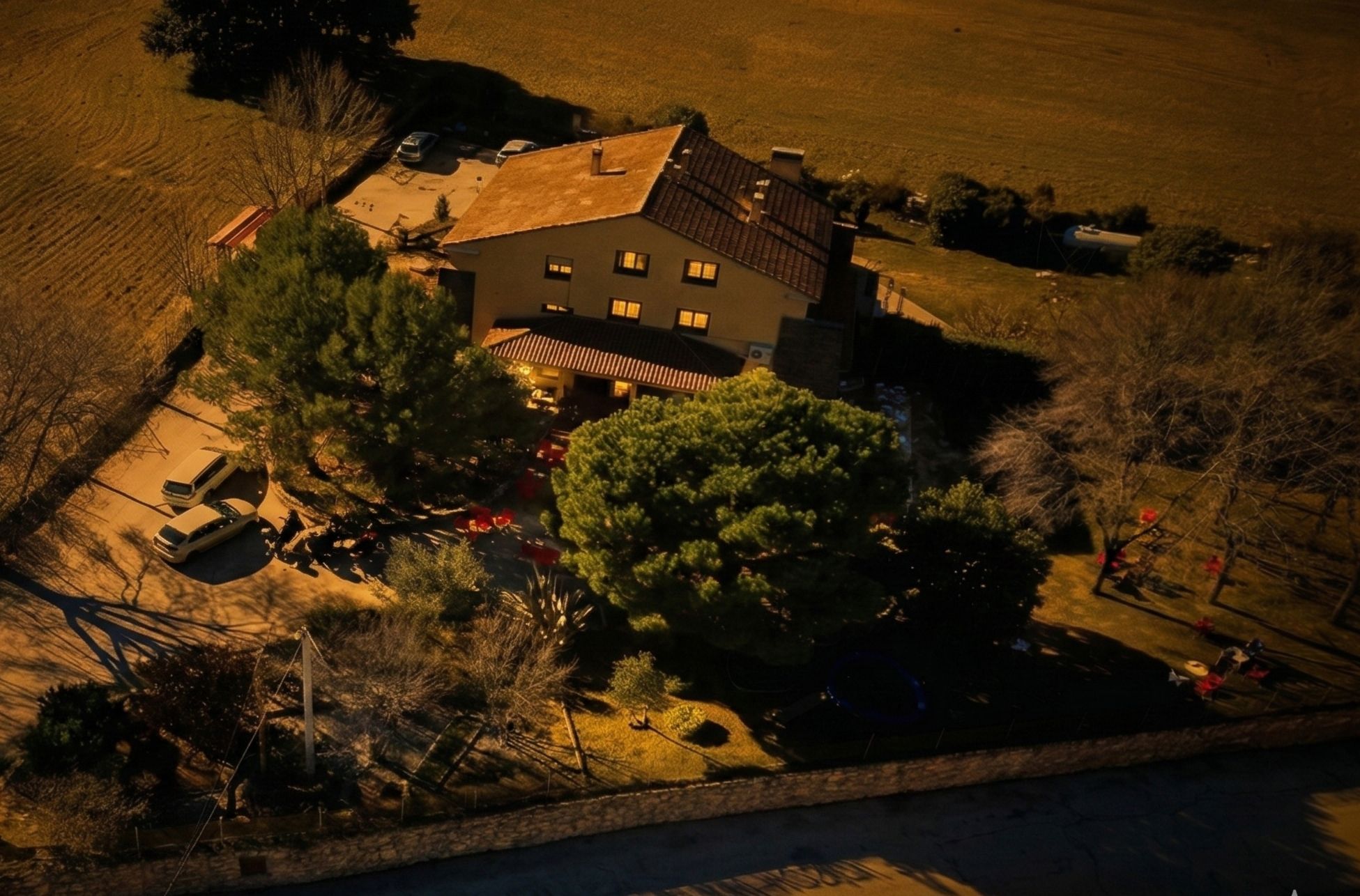 An aerial view of a two-story house with a sloped roof, surrounded by a well-maintained lawn and a few trees.