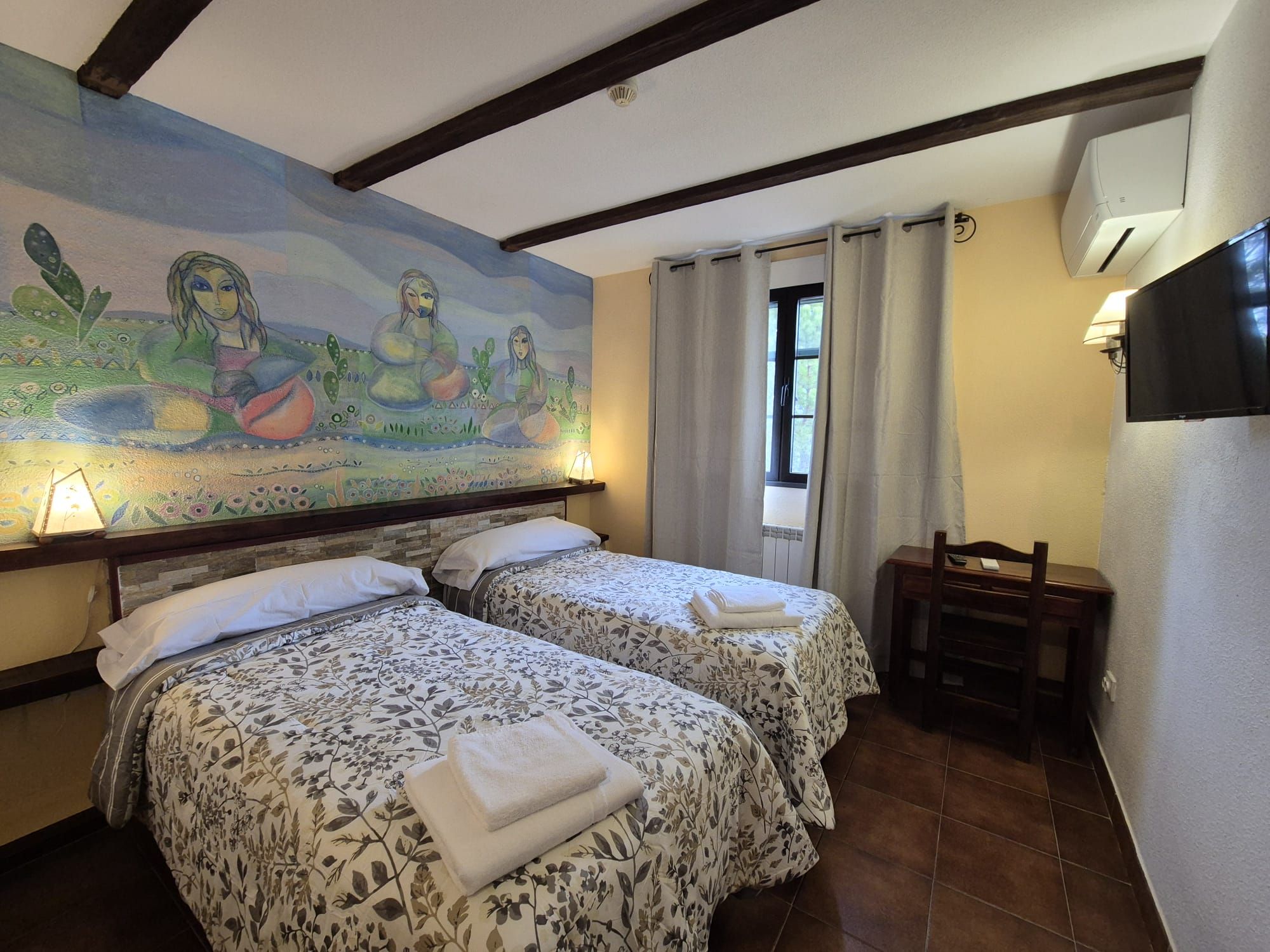 A hotel room with two beds, a mural on the wall, a TV, and a window with curtains.