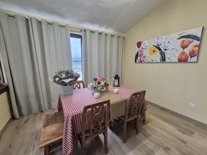 Un coin repas avec une nappe à carreaux, des chaises en bois, un vase de fleurs et un tableau accroché au mur.